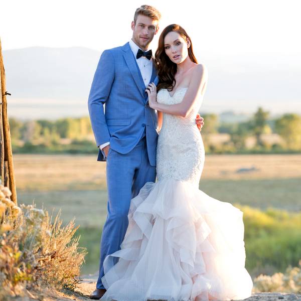 Bride and groom posing in field in blue tuxedo and white dress
